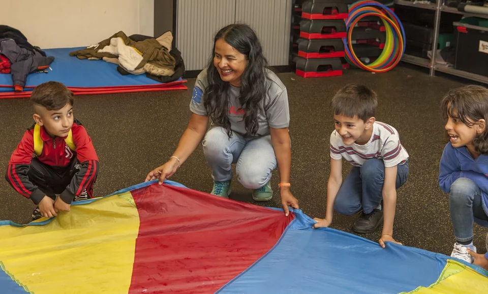 Begeleider met kinderen die bij een gekleurd kleed staan